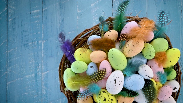 复活节彩蛋在一个巢与彩色羽毛转向蓝色木制背景视频下载