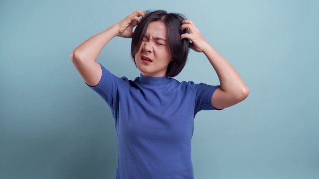 亚洲妇女的肖像抓她的头孤立在蓝色的背景。4 k的视频视频下载