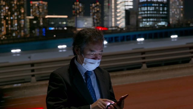 日本中年工薪族戴着面具，晚上在东京街头用智能手机发短信视频下载