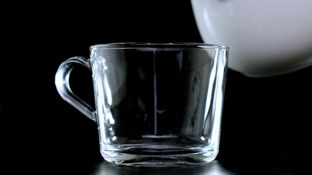 把牛奶倒在一个透明的杯子里，背景是黑色的。关闭了。视频下载