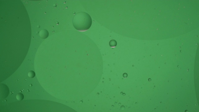 绿色球体油泡在液体中顺时针循环运动，气泡微距拍摄。抽象智能手机主屏幕保护程序风格，主题或背景，绿色背景视频素材