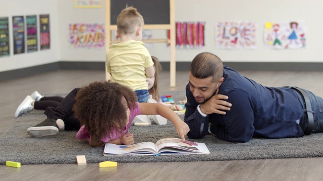 一个幼儿园老师和一个小女孩一起读书的慢动作镜头视频素材