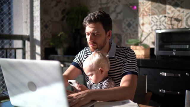 一名男子抱着儿子在家用笔记本电脑工作视频下载