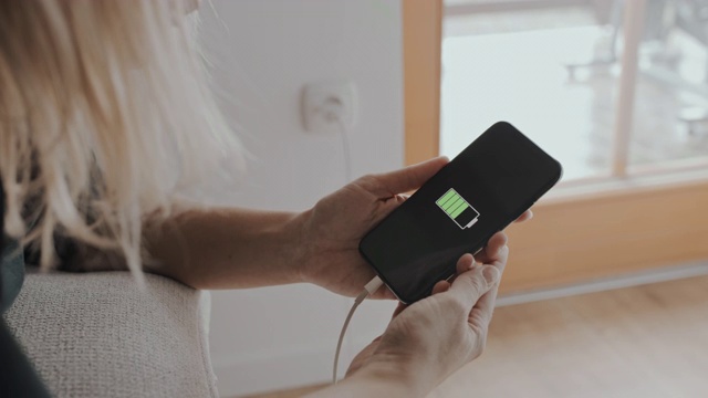 一个女人正在用手机充电器连接一个空的智能手机视频下载