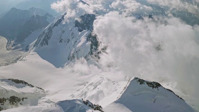 神奇的高山全景，登山运动员攀登在雪崖上，云漂浮在山顶下视频素材