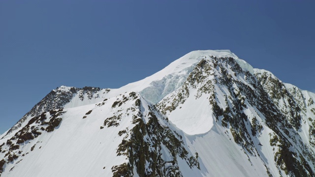 无人机绕着完美的雪白色山顶在蓝天上闪耀视频素材