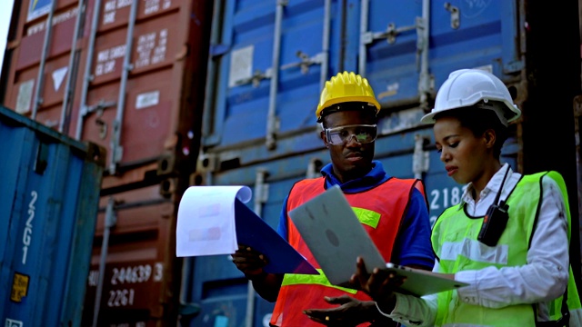 两名非洲工程师戴着安全帽，手持笔记本电脑和剪贴板在集装箱堆场前检查集装箱视频素材