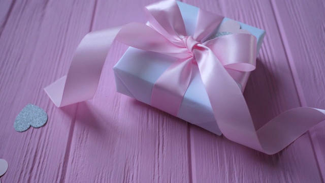 礼盒与丝带和纸屑的形式的心在粉红色的木制背景与地方为您的文本。视频在情人节，母亲节或生日。顶视图高清视频下载