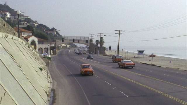 东面面向南太平洋海岸高速公路(pch)，圣塔莫尼卡北部交通温和/左海滩看山在右/ CAM平移l-r与大型2门1970年的蓝色轿车/ neg切到相同的镜头面对北CAM平移r-l与相同的轿车视频下载