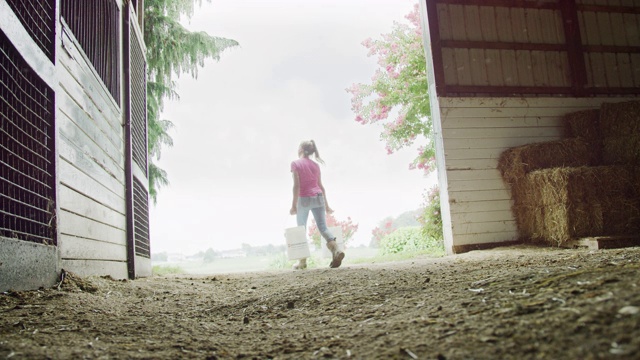 一名年轻女子穿着工作靴从农场谷仓里拎出5加仑桶的慢动作镜头视频素材