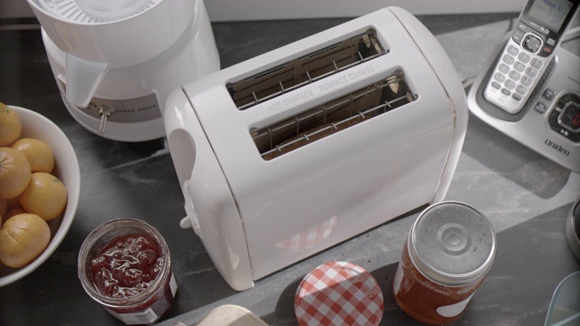 厨房烤面包机手动按钮高向下角度。电话，榨汁机和罐子果酱可见。视频下载