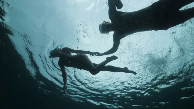 一对在水下浮潜的情侣在强光下一起游泳。视频下载