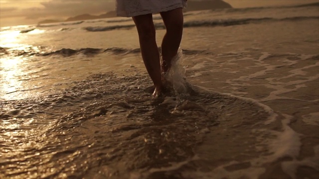 美丽的场景，一个低段的女人走在海边的日落视频素材