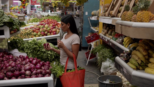 年轻的拉丁美洲妇女购买新鲜蔬菜和水果，并将它们放入可重复使用的袋子视频素材