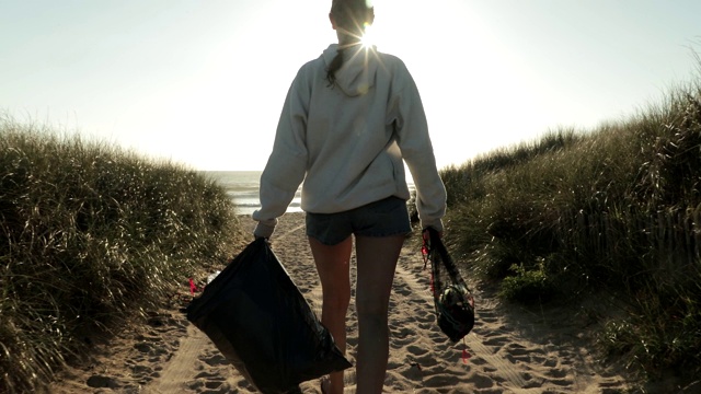 女孩在日落时分清理海滩上的塑料和垃圾视频下载