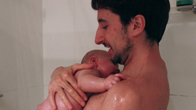爸爸抱着婴儿在淋浴，给新生儿洗澡视频素材