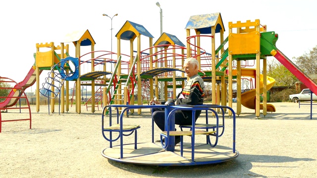 一个老人在空旷的操场上骑着儿童旋转木马视频下载
