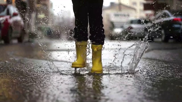 穿着黄色橡胶靴子的孩子的腿在水坑里跳视频下载