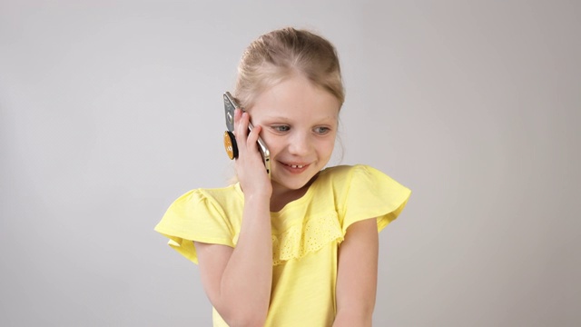 一个小女孩正在打电话，白色背景下穿着一件亮黄色连衣裙。一个小女孩在电话里情绪化的谈话。视频素材