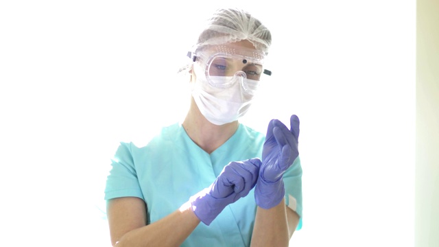 戴医用口罩和安全眼镜的护士戴一次性手套。医务人员的个人保护视频下载