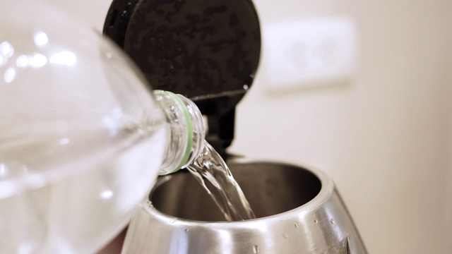 一个人的手把水从瓶子倒进厨房的电水壶里。视频素材