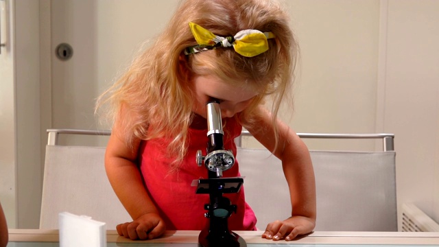穿粉红色衣服的金发小女孩正在透过显微镜镜头看东西视频下载
