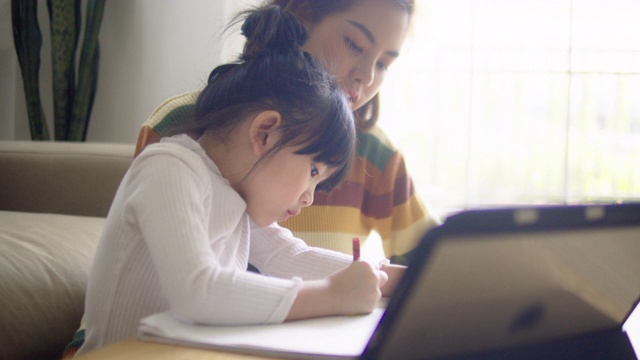 年轻的母亲和女儿在家里用平板电脑做作业。视频下载
