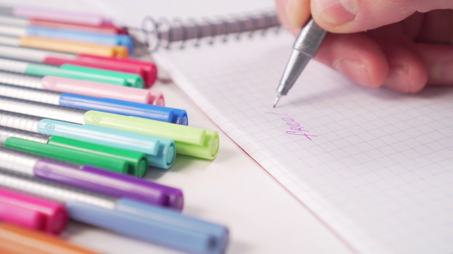 Hand用灰色钢笔用红墨水在笔记本上写字。旁边的桌子上有几支彩色毡头笔视频下载