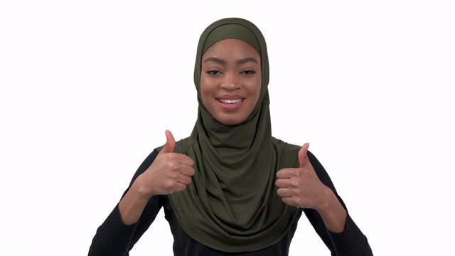 穆斯林深色皮肤的女模特在希贾布显示她的大拇指向上和微笑。肢体语言和手势。孤立的,白色背景视频下载