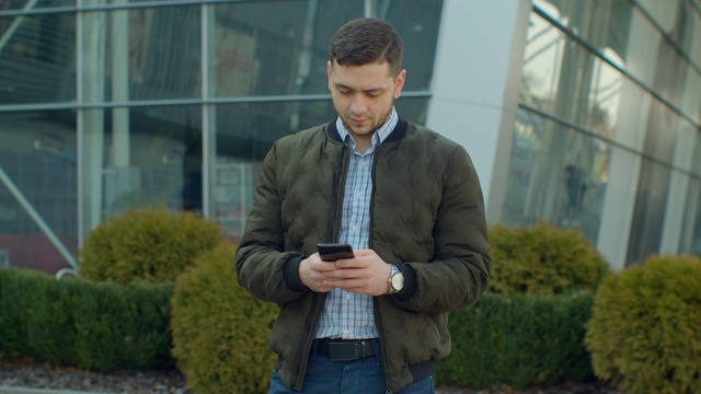 年轻人在城市的街道上使用手机，打字，与朋友聊天，男人在户外使用手机。视频素材