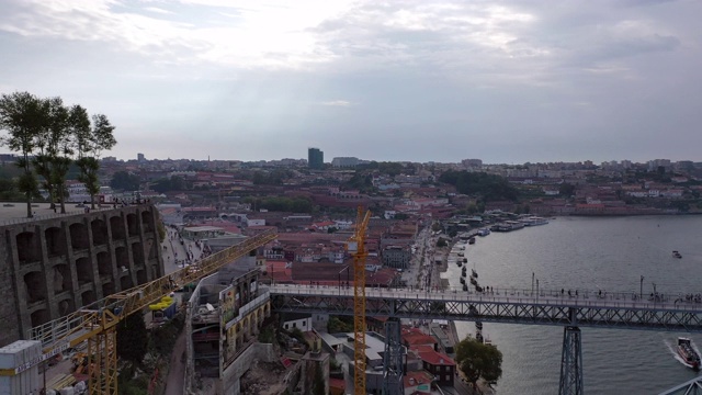 航拍河上著名的桥，城市里的建筑物，无人机向后飞行，在多云的天空附近的起重机-波尔图，葡萄牙视频下载