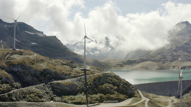 航拍的风力涡轮机山上的冰川湖，无人机向后飞行的景观对天空在阳光明媚的一天-瑞士阿尔卑斯山，瑞士视频下载