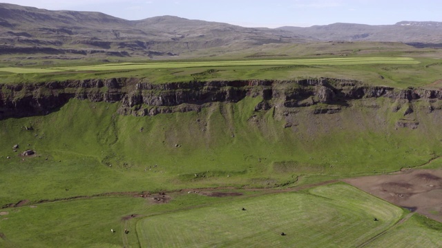 在晴朗的日子里，无人机在冰岛西南部的自然景观上空拍摄悬崖边的绿色农田视频下载