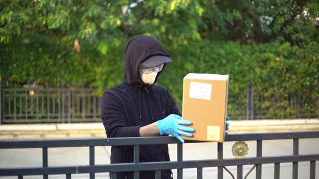 快递员戴上安全眼镜和面罩，将包裹放在围栏上，保持距离，减少细菌传播视频下载