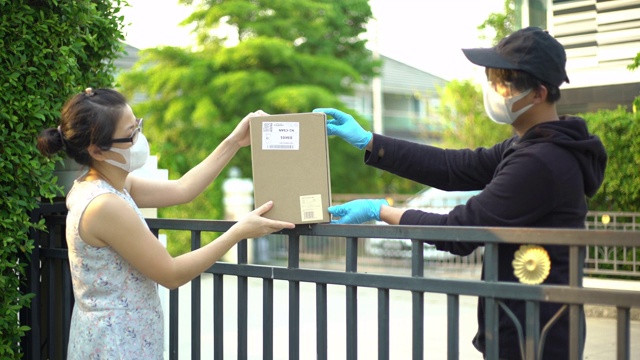 一名亚洲妇女从戴口罩和手套的快递员手中接过包裹，以防止新冠肺炎视频下载