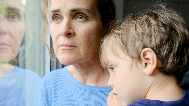 一名成熟女子和儿子合影，非常悲伤地透过窗户向外看，担心2019冠状病毒病被封锁视频素材