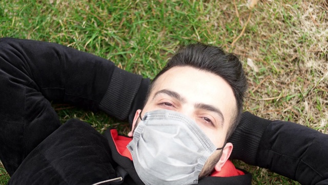 一个戴着医用口罩的病人的肖像，背景是一个城市公园。视频素材