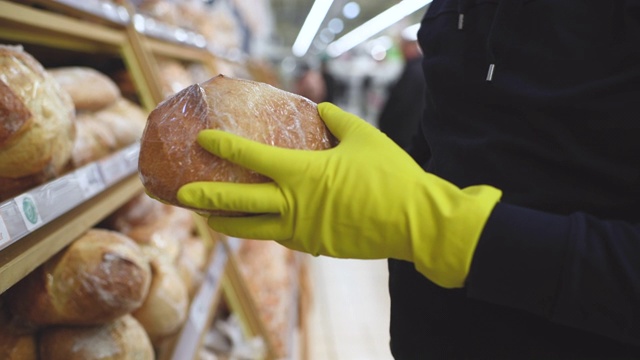戴着面具和橡胶手套的男人在超市挑选面包视频素材