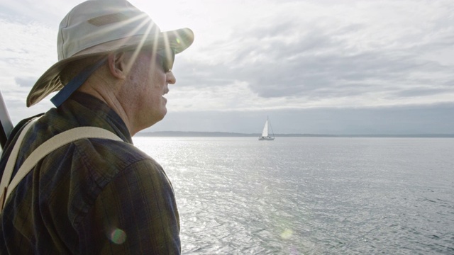 一名六十多岁的男子在多云的一天从一艘帆船的甲板上俯瞰华盛顿普吉特海湾的慢动作镜头视频素材