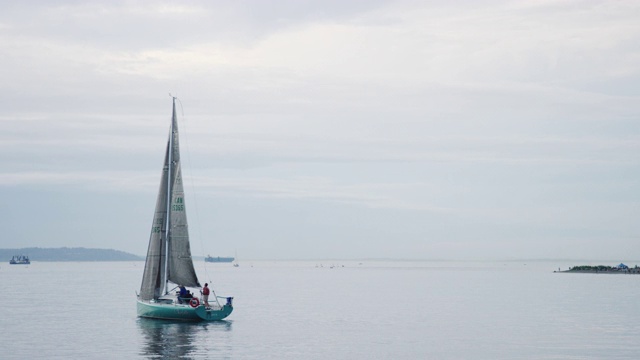 一艘帆船与一个小船员在一个阴天驶进华盛顿的普吉特海湾的慢动作拍摄视频素材