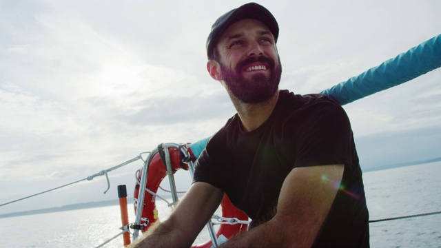 慢动作拍摄的一个白人男子在他的30岁微笑，因为他坐在一艘帆船的甲板上在普吉特海湾在华盛顿多云的一天视频素材