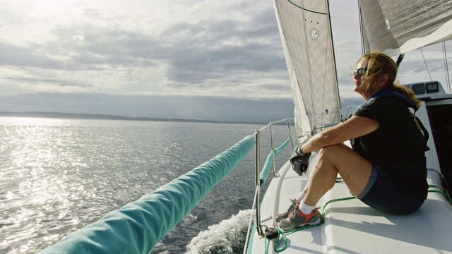一个六十多岁的女人在多云的一天坐在一艘帆船的甲板上俯瞰华盛顿的普吉特海湾的慢动作镜头视频素材