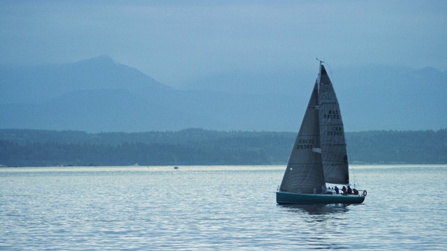 一艘帆船与一个小船员在一个阴天驶进华盛顿的普吉特海湾的慢动作拍摄视频素材