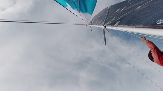 一个多云的日子，华盛顿普吉特海湾，一名60多岁的帆船船长正在吊起他的帆船上的三角帆视频素材