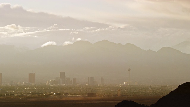 云在拉斯维加斯城市天际线上滚动的时间流逝与山在一个朦胧的日子背景，而沙尘暴吹过沙漠在日落的前景视频下载