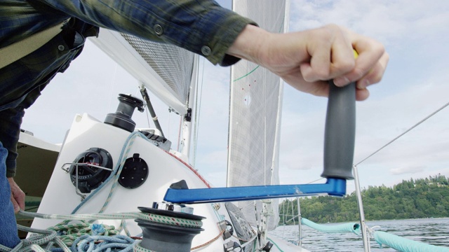 一个六十多岁的男人在一艘帆船的甲板上转动绞车手柄的慢动作镜头，华盛顿州西雅图附近的普吉特海湾视频素材