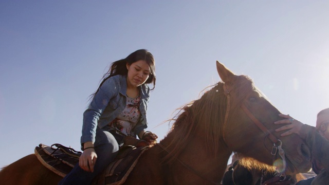 一个印第安人(纳瓦霍人)女孩在她的十几岁骑她的马，而另一个女人平静的马在一个明亮的，阳光明媚的一天在亚利桑那州的沙漠视频下载