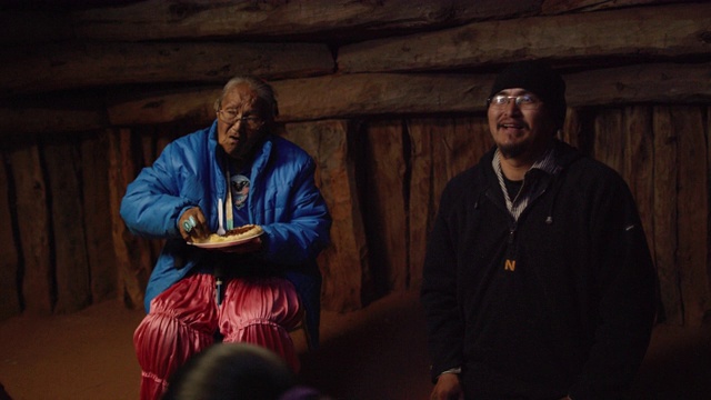 一位美国土著(纳瓦霍人)妇女将豆子舀到玉米饼(炸面包)上，而她的不同年龄的家庭成员在木制的Hogan(纳瓦霍人小屋)内一起聊天、吃饭和大笑。视频下载