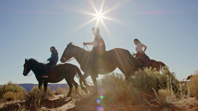 几个年轻的印第安人(纳瓦霍)孩子骑着马穿过纪念碑谷沙漠和他们的宠物狗在亚利桑那州/犹他州在一个晴朗，明亮的日子视频下载