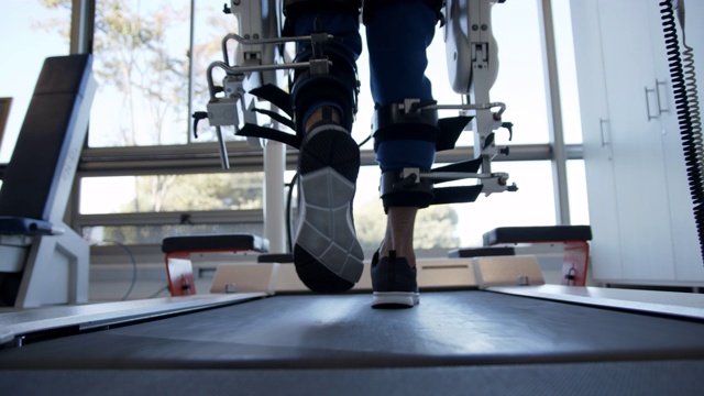 特写的人在跑步机上行走的帮助下，外骨骼机器人在一个康复诊所视频下载
